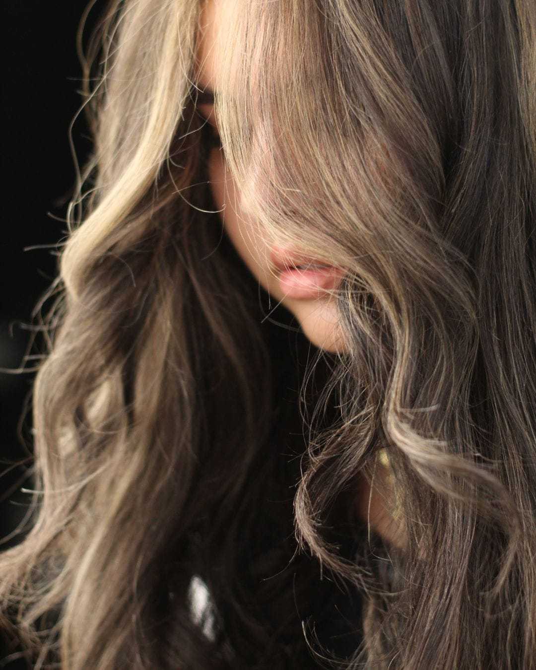 Wavy brown hair with highlights partially covers face in soft lighting.
