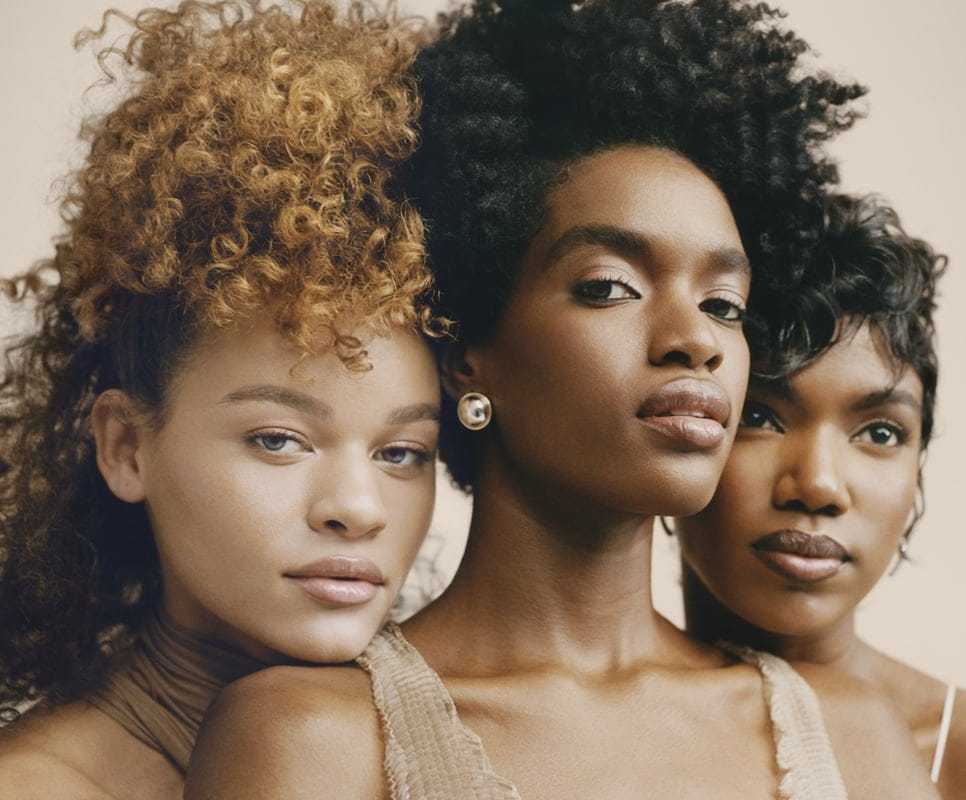 Three women with diverse hairstyles pose confidently.