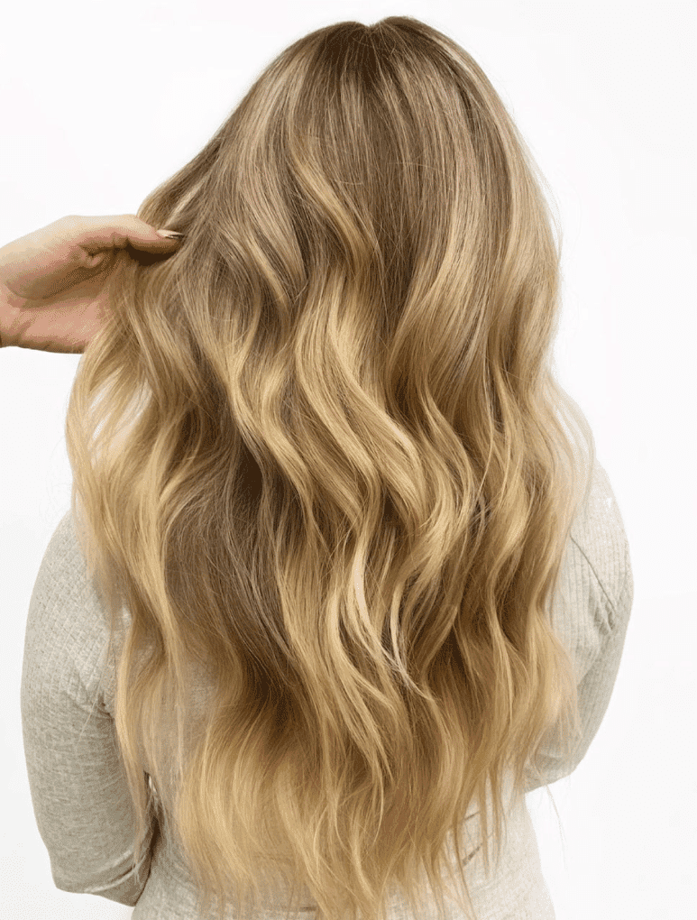 Long, wavy blonde hair with balayage highlights being styled by a hand.