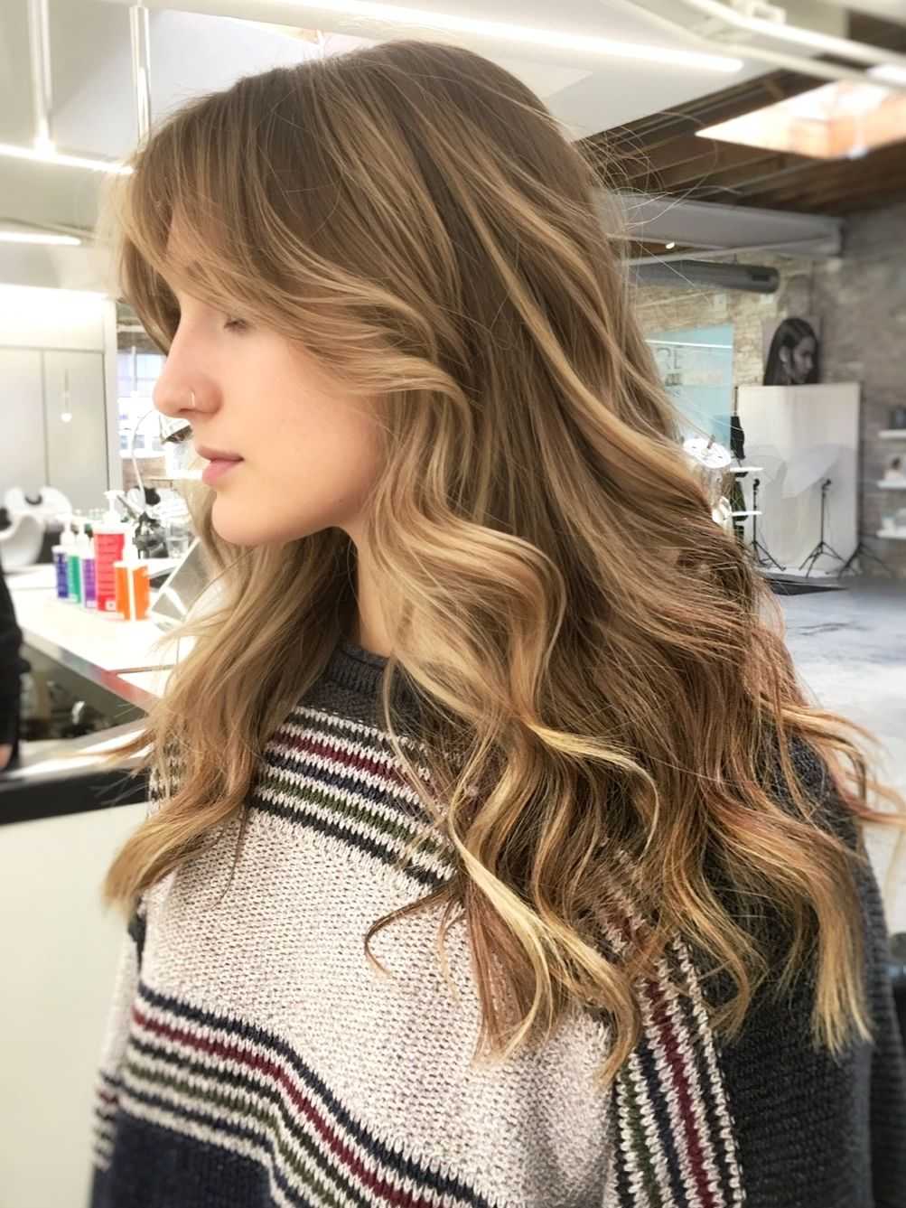 Woman with long wavy blonde hair in a salon, wearing a striped sweater.